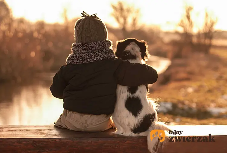 Dziecko z psem siedzący nad stawem, a także jak pogodzić dziecko i psa oraz kontakty między psem a dzieckiem krok po kroku