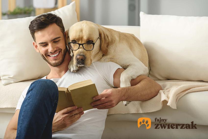 Pies w okularach spoglądający przez ramię mężczyzny na trzymaną przez niego w rękach książkę, bezwarynkowa miłość psów zawarta w cytatach
