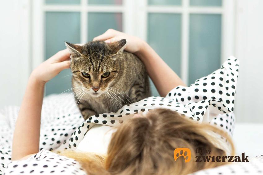 Kobieta leżąca w łóżku tuląca się do kota, a także informacje, czy koty leczą depresję oraz inne dolegliwości